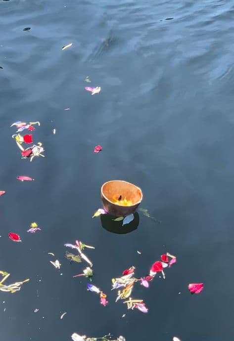 A lit diya floating among flower petals on the river